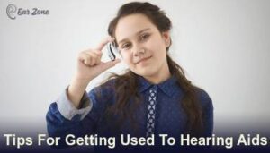 Featured image of a girl holding a hearing aid. Article on tips for getting used to hearing aids